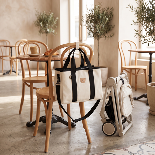 Diaper Tote Bag for Moms, on a cafe chair next to a stroller