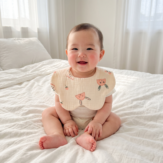 Muslin Baby Bib, worn by a smiling baby sitting on a bed