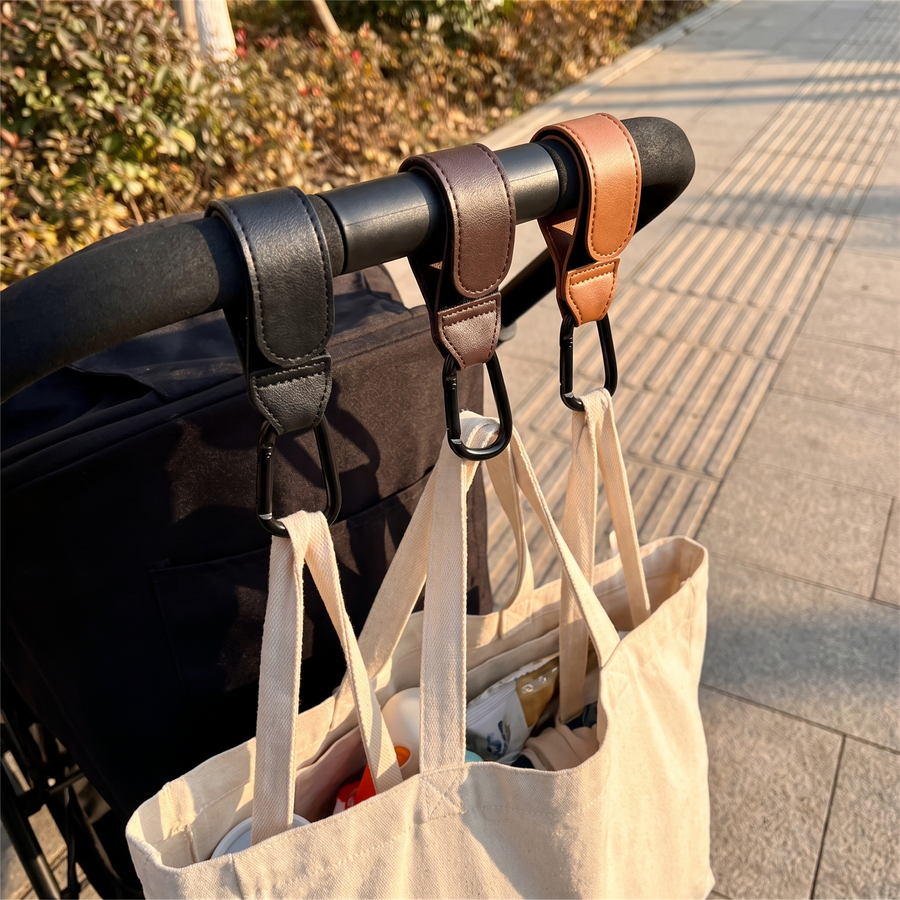 Stroller Hooks, clipped to a stroller handle holding a tote bag, on a sidewalk